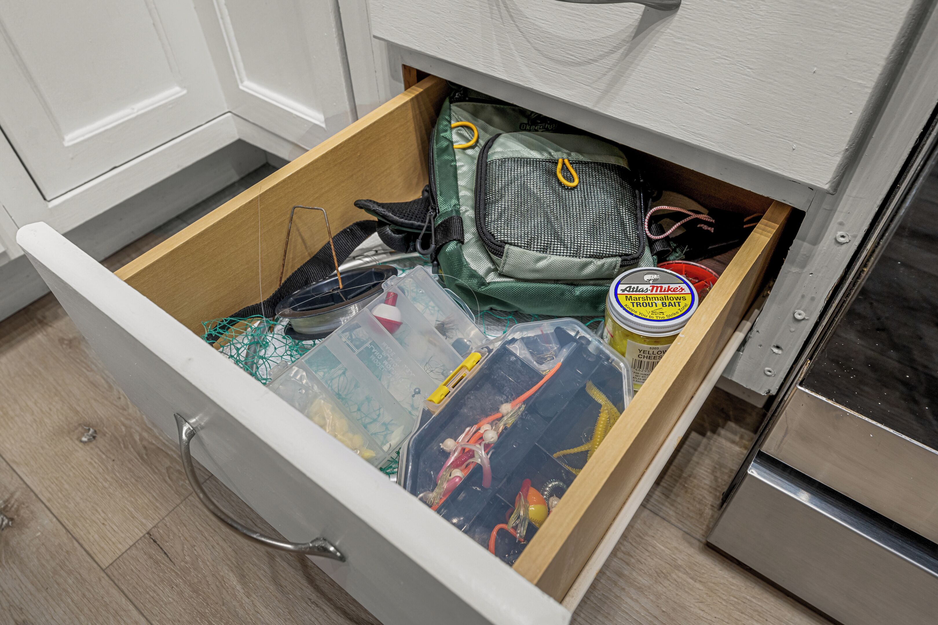 Un tiroir de cuisine rempli de divers objets, notamment un sac vert, une boîte de conserve de poisson et quelques récipients en plastique.
