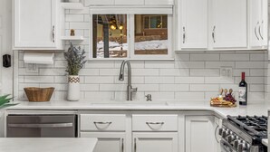 A modern kitchen with white cabinetry, a stainless steel sink, and a window with a view of a snowy landscape. - Right on the River! Mtn Cabin w/ Deck & Fireplace (Shawnee)