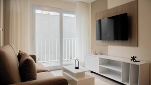 A modern living room with a sofa, a coffee table, a TV, and a sliding glass door leading to a balcony.