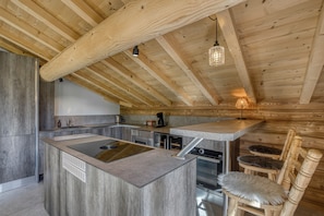 A modern kitchen with wooden beams, a central island, and a dining area with wooden chairs.