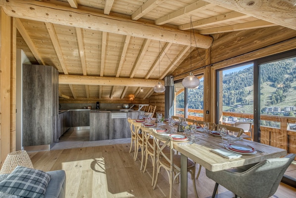 A wooden interior with a dining area, kitchen, and large windows offering a mountain view.