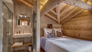 A bedroom with a wooden ceiling, a bed with white bedding, and a bathroom with a glass shower enclosure. - "Borderan" Apartment with Mountain Views, Jacuzzi, Balcony, and Wi-Fi (La Clusaz)
