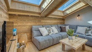 A room with a grey sofa, a wooden coffee table, a TV, and a skylight. - "Borderan" Apartment with Mountain Views, Jacuzzi, Balcony, and Wi-Fi (La Clusaz)