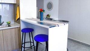 Una cocina moderna con encimera blanca, dos taburetes azules en la barra, un lavamanos y un florero con flores sobre la encimera.