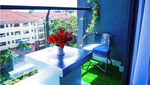 Un balcón con una silla, una mesita con un florero y vistas a edificios y zonas verdes.