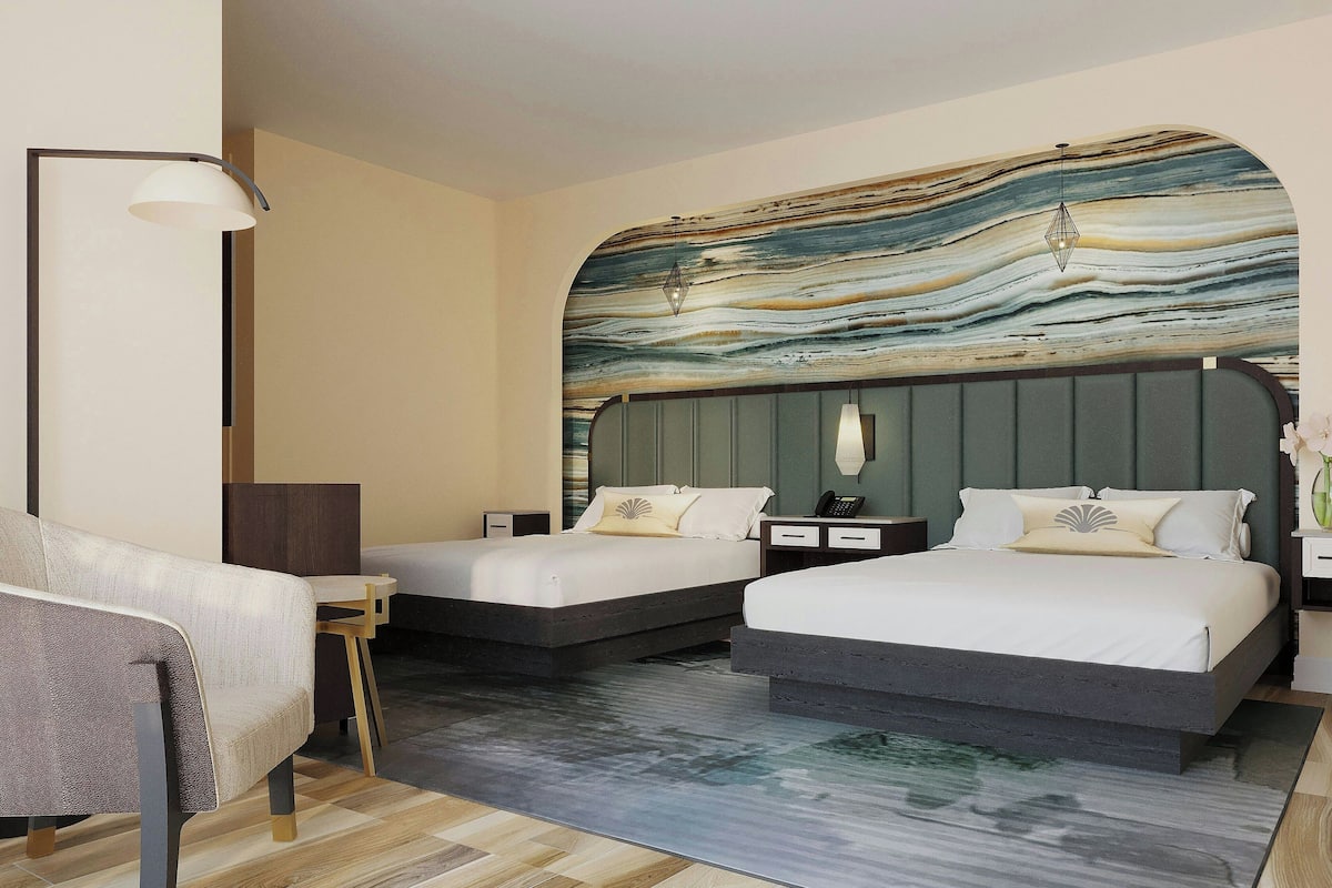A hotel room with two beds, a sofa, a desk, and a large wall mural.