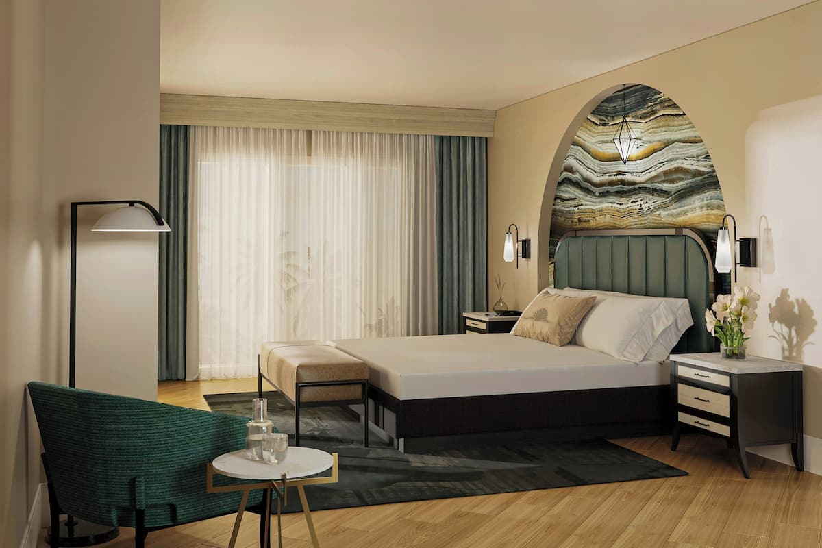 A modern hotel room with a large bed, a desk, a chair, a floor lamp, and a view of the city through the window.