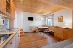 Una cocina con armarios de madera, una mesa de comedor y un televisor montado en la pared.