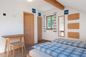 Quarto com escrivaninha de madeira, cama com colcha xadrez azul e branca, janela com cortinas e decorações de parede em madeira.