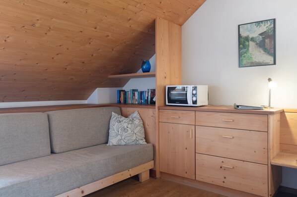 A wooden ceiling, a sofa with a patterned pillow, a wooden cabinet with drawers, a microwave, and a framed picture on the wall.