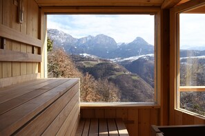 A wooden cabin with a bench and a large window offering a mountain view.