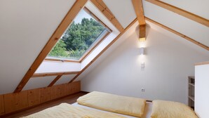 Une petite chambre mansardée avec un puits de lumière, des poutres en bois et un mur blanc.