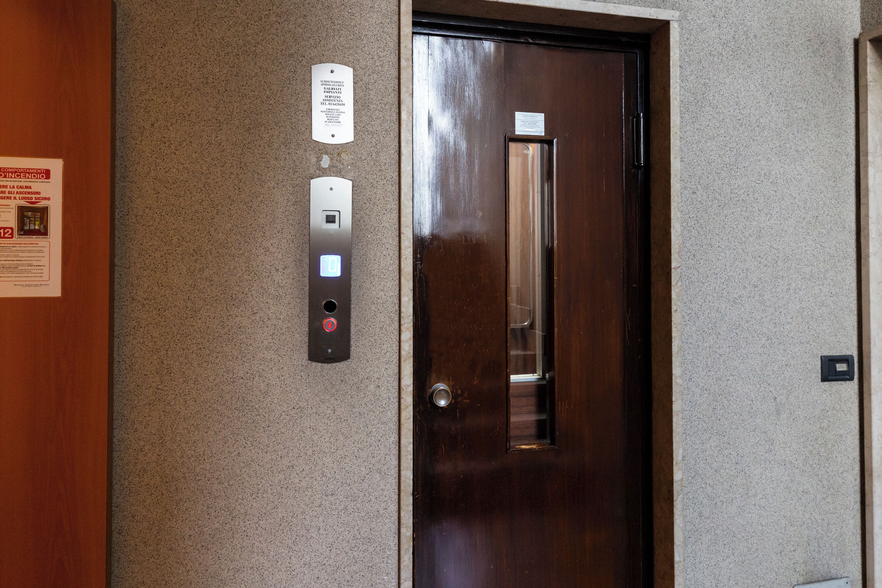 An elevator with a control panel, a door, and a wall-mounted sign.