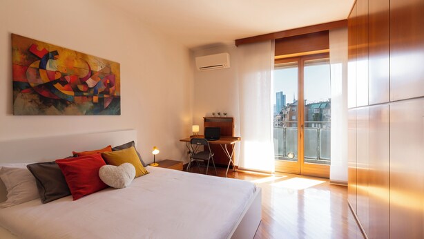 A hotel room with a bed, a desk, a chair, a TV, and a large window with a city view. - notaMi - Simply Six (Milan)