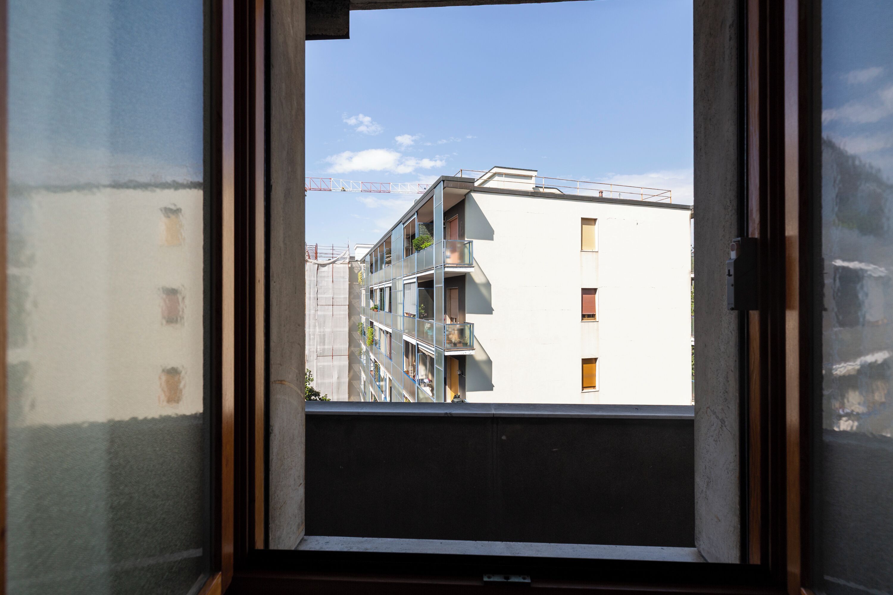 A view through a window of a multi-story building with balconies and a construction crane in the background.