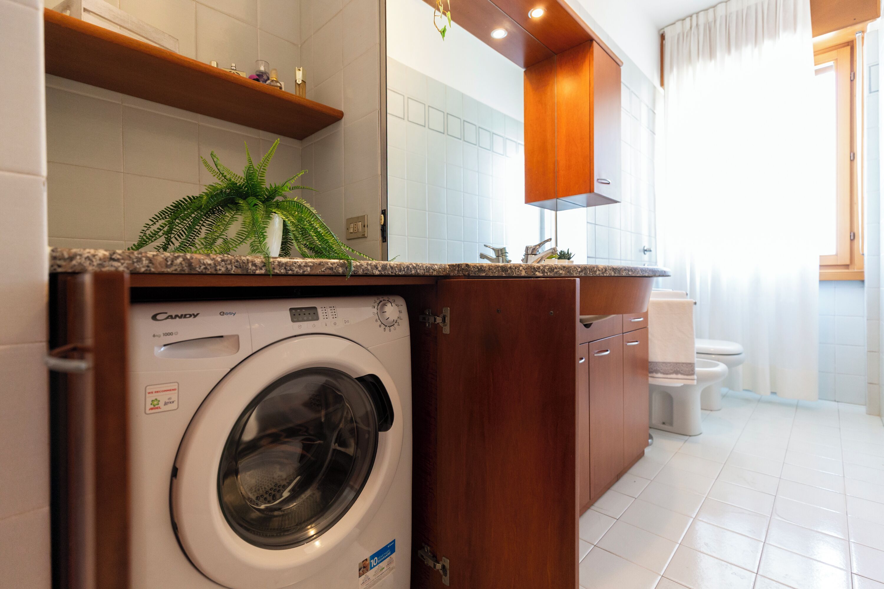 A compact, modern bathroom with a built-in washing machine, a toilet, and a shower area.