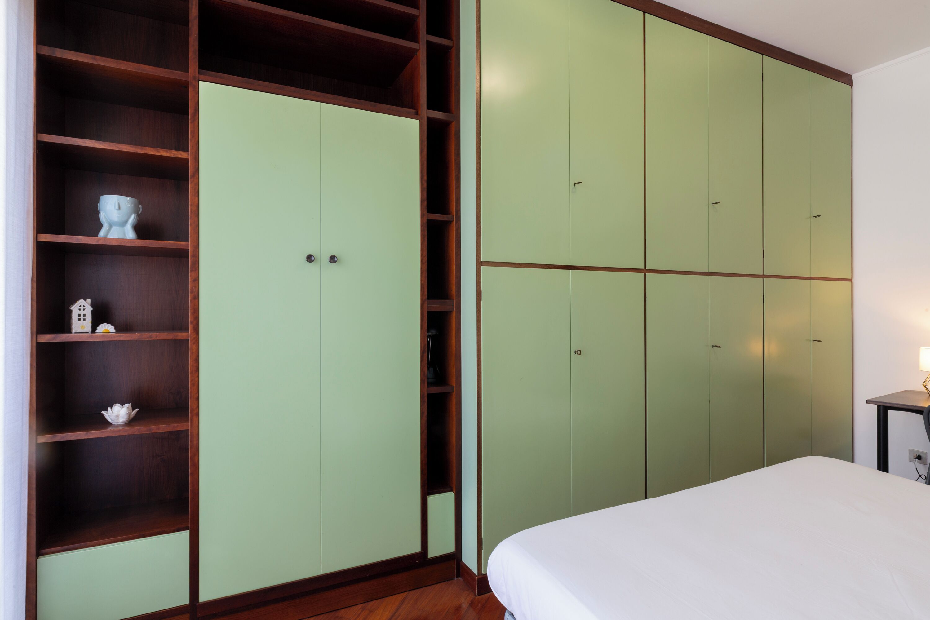 Ein Schlafzimmer mit einem Bett, einem grünen Kleiderschrank und einer Holzhängeregal mit Dekorationen.