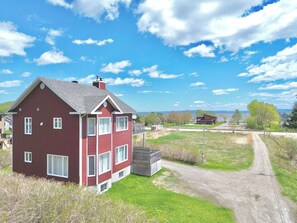 A red house with a grey roof, a small shed, and a dirt road leading to a body of water.