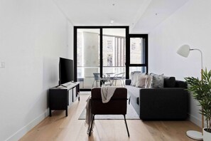 Ein modernes Wohnzimmer mit einer Couch, einem Fernseher, einem kleinen Tisch und einer Pflanze.