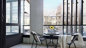 A balcony with a table and chairs, a window with a sunflower decoration, and a view of buildings. - A Cozy 2BR Apt Right on Buzzing Chapel Street (South Yarra)