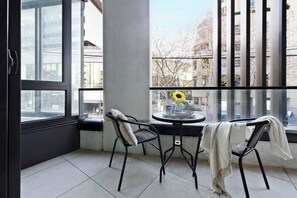 Ein Balkon mit Tisch und Stühlen, ein Fenster mit Sonnenblumen-Dekoration und Blick auf Gebäude.