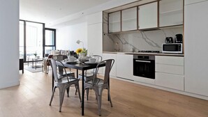 A modern kitchen with white cabinetry, a marble backsplash, and a dining area with metal chairs and a table set for four. - A Cozy 2BR Apt Right on Buzzing Chapel Street (South Yarra)