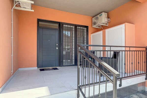 A building entrance with a metal staircase, a door with a window, and an air conditioning unit on the wall. - AMINA Guest House (Fiumicino)