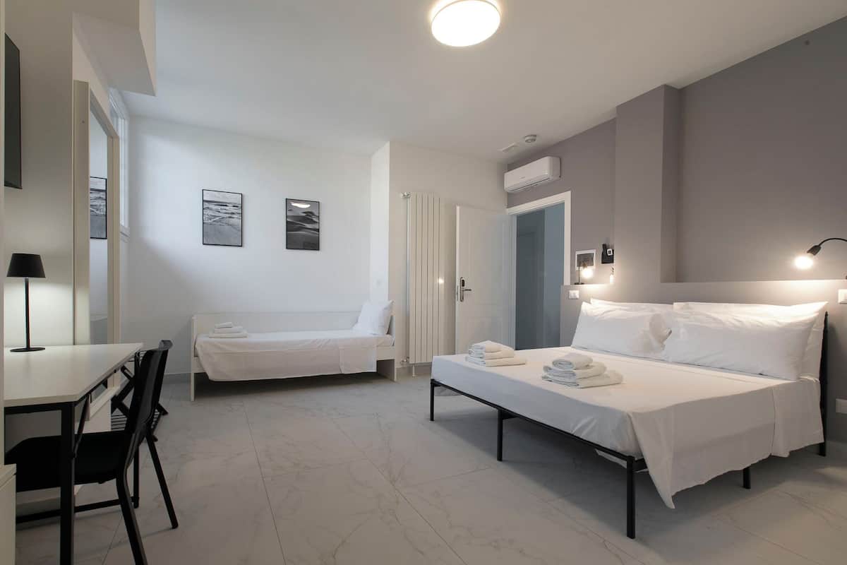 A modern, well-lit room with two beds, a desk, and a chair.