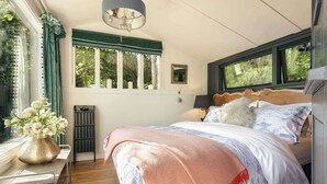 A bedroom with a bed, a bedside table, a lamp, a window, and a view of trees.