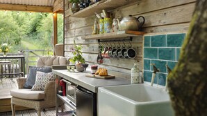 A rustic kitchen with wooden shelves, hanging pots, and a view of greenery outside.