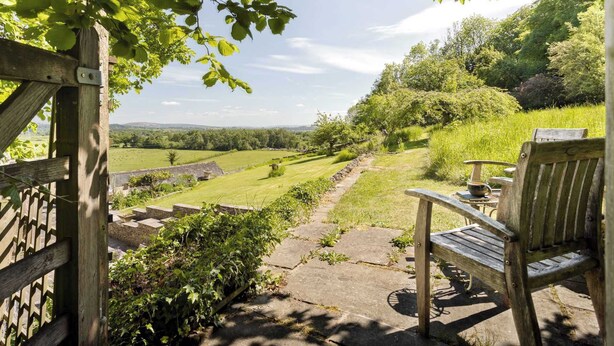 A wooden bench and table set on a stone pathway overlooking a lush green landscape with a clear sky.