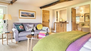 A cozy living room with a sofa, a coffee table with books and a bottle, a lamp, and a painting on the wall.