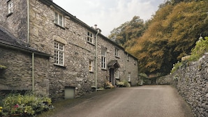 A stone building with a cobblestone driveway, surrounded by lush greenery and trees.