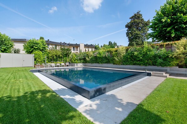 A rectangular swimming pool with a tiled deck, surrounded by well-maintained grass and trees.