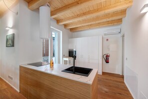 A modern kitchen with a wooden ceiling, white cabinets, a black sink, and a fire extinguisher.