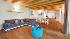 A modern living room with a sectional sofa, a teal bean bag, wooden flooring, and a kitchen in the background.