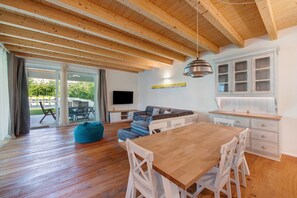 A spacious living area with a wooden ceiling, a dining table, and a kitchen with white cabinets.