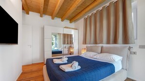 A bedroom with a bed, a mirror, a television, and wooden flooring.