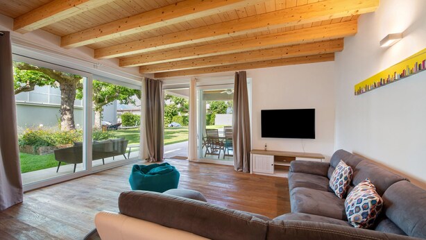 A modern living room with a wooden ceiling, a large window, a sofa, and a flat-screen TV.