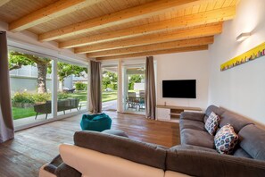 A modern living room with a wooden ceiling, a large window, a sofa, and a flat-screen TV. - Villa 'Carlotta' - Porto Portese with private pool, private terrace and air conditioning (Portese)