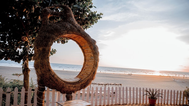 Une scène de plage avec une structure en forme de miroir circulaire, une clôture blanche en bois et un banc.