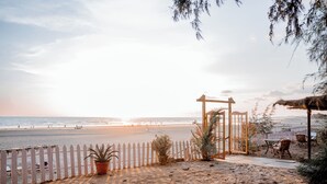 Une vue sur la plage avec une clôture en bois, des plantes en pot et du mobilier d’extérieur.