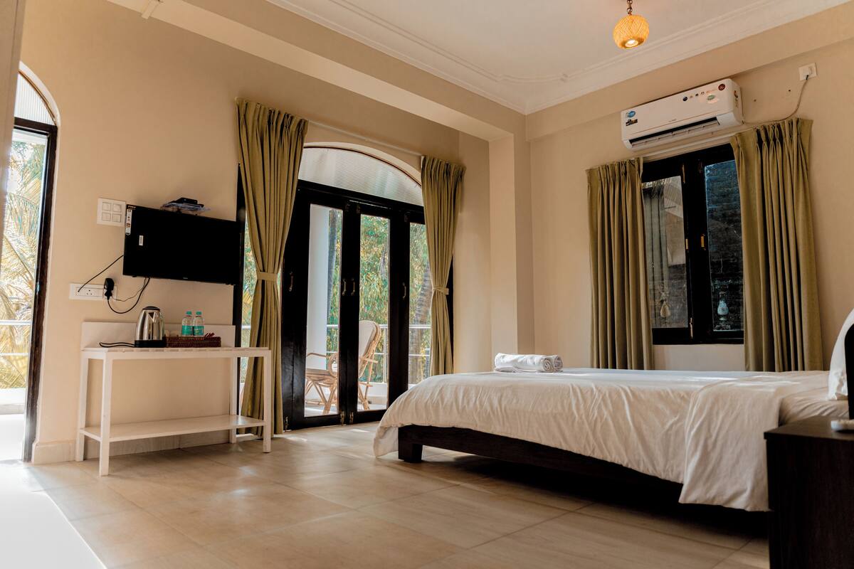 A bedroom with a bed, a desk, a television, and an air conditioning unit.