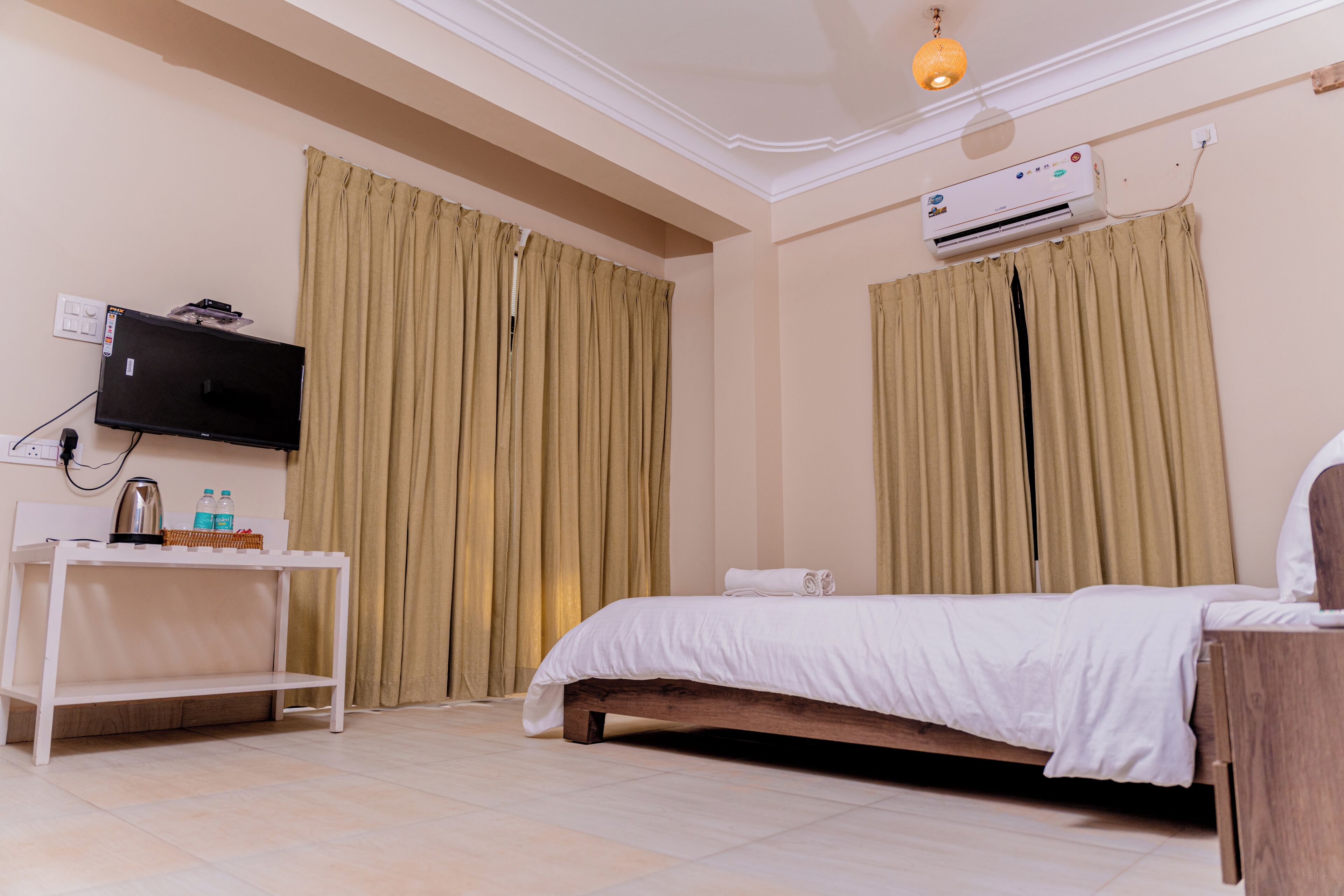 Een hotelkamer met een bed, een televisie op een standaard, een airconditioner en gordijnen.