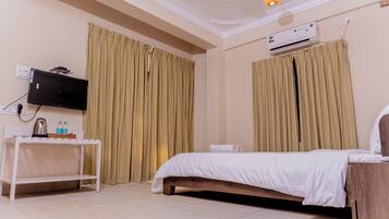 Een hotelkamer met een bed, een televisie op een standaard, een airconditioner en gordijnen.