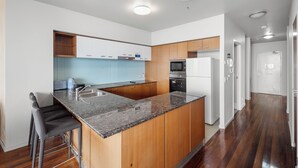 A modern kitchen with granite countertops, wooden cabinets, a built-in island with bar stools, stainless steel appliances, and recessed ceiling lighting.