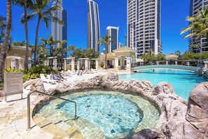 A resort pool with clear water, surrounded by palm trees and modern high-rise buildings in the background. - Chevron Renaissance - 2421 (3BR/2BA) (Gold Coast)