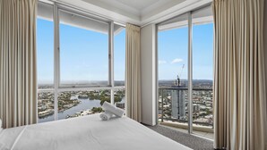 A hotel room with a large bed, beige curtains, and a city view through floor-to-ceiling windows.