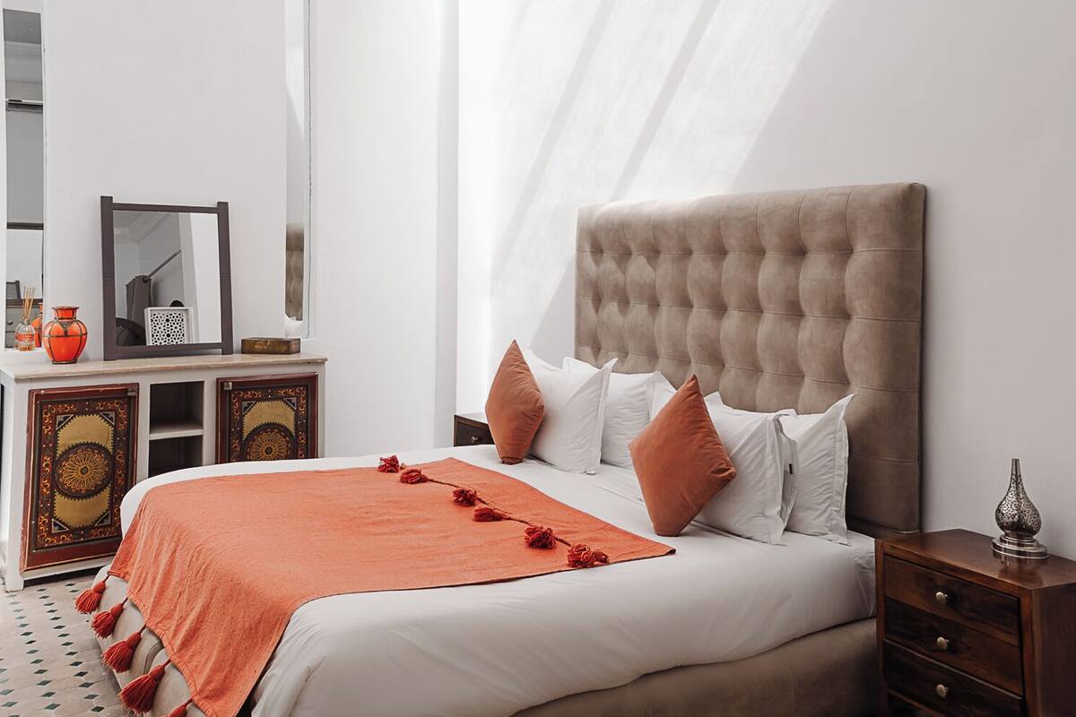 A bedroom with a large bed, a nightstand, a mirror, and a patterned rug.