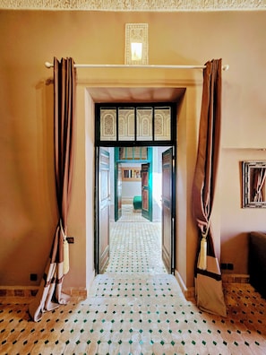 A hallway with patterned floor tiles, a doorway with decorative panels, and curtains on either side. - Le Riad Medina Privilège & Spa (Marrakech)